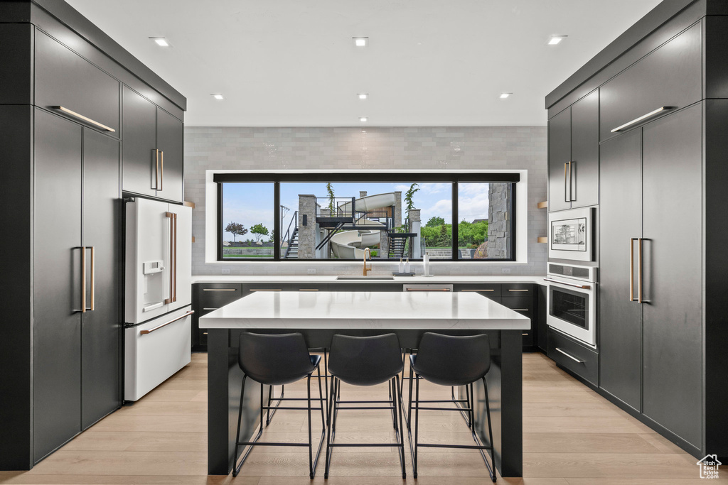 Kitchen with white appliances, a breakfast bar area, a kitchen island, tasteful backsplash, and light countertops