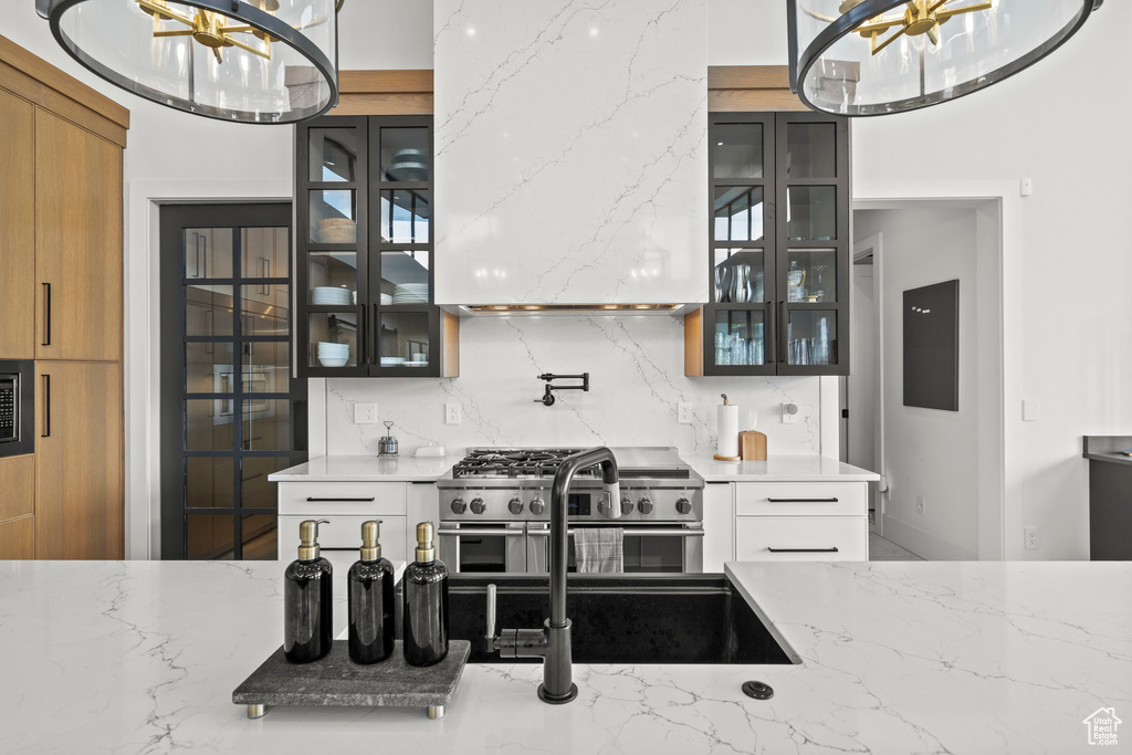 Kitchen with high end stainless steel range oven, glass insert cabinets, light stone countertops, and wall chimney range hood