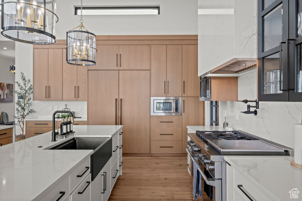 Kitchen with appliances with stainless steel finishes, a sink, light brown cabinets, a chandelier, and light wood-style floors