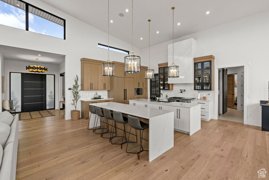 Kitchen with a large island, a towering ceiling, light wood-style flooring, backsplash, and pendant lighting