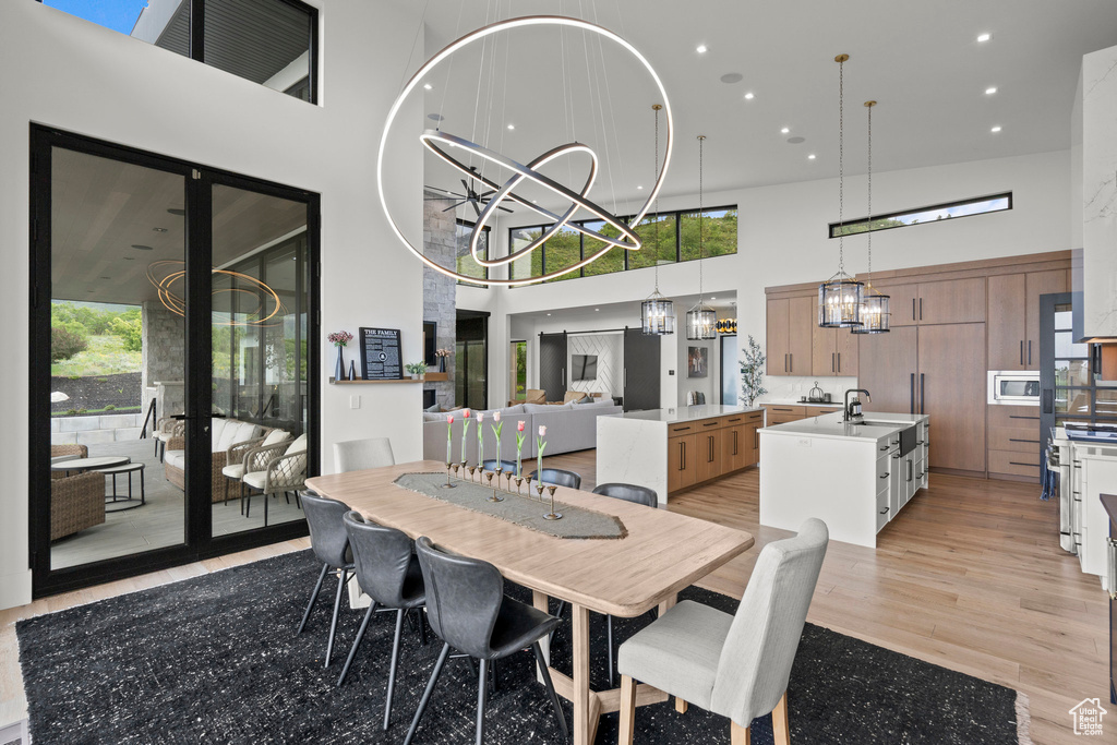 Dining space with a towering ceiling, a chandelier, recessed lighting, and light wood-style flooring