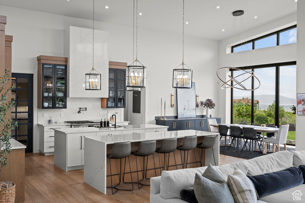 Kitchen featuring a large island with sink, a chandelier, open floor plan, light wood-style floors, and a towering ceiling