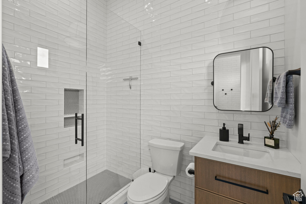 Bathroom with a shower stall, vanity, toilet, and tile walls