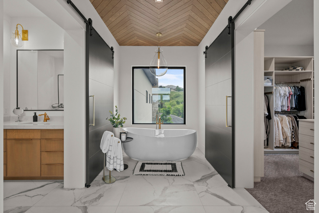 Bathroom featuring vanity, a walk in closet, a freestanding tub, vaulted ceiling, and marble finish flooring