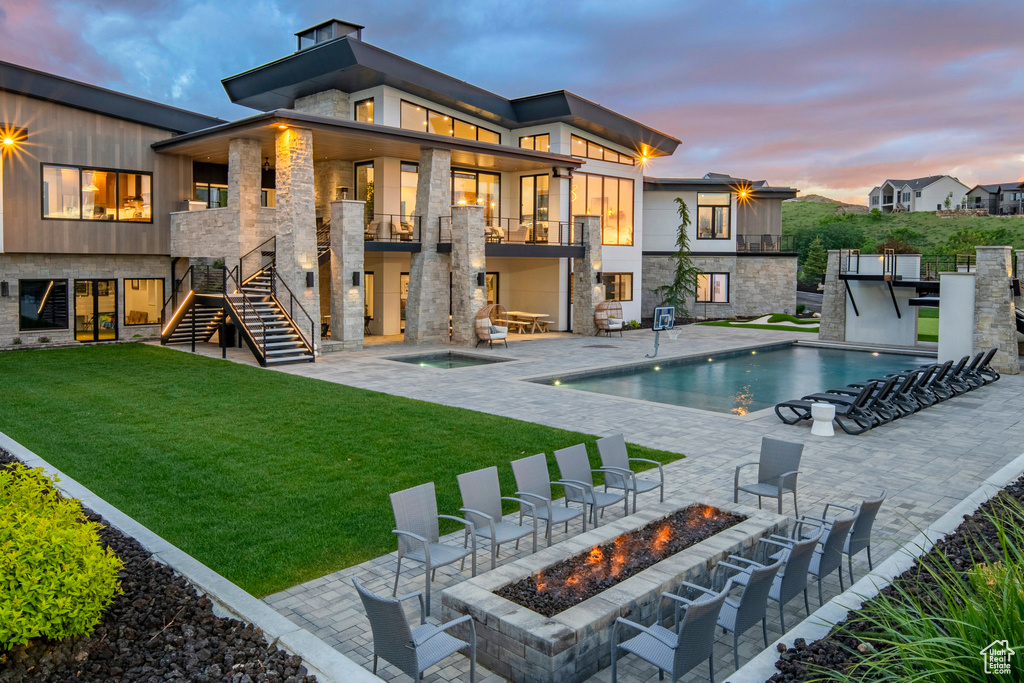 Back of property featuring a fire pit, a balcony, an in-ground hot tub, stairway, and a lawn