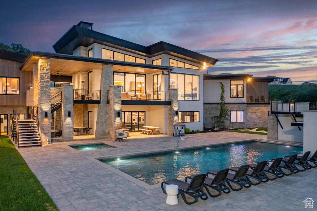 Back of property featuring a balcony, a patio area, an in-ground hot tub, and stone siding