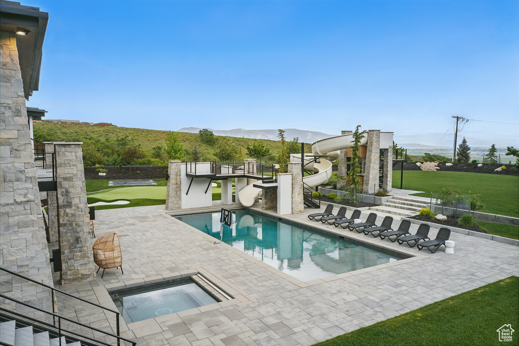 View of pool featuring a water slide, an in-ground hot tub, a patio, and a mountain view