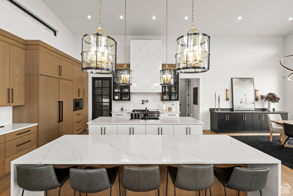 Kitchen with a spacious island, a chandelier, built in appliances, brown cabinetry, and a breakfast bar area