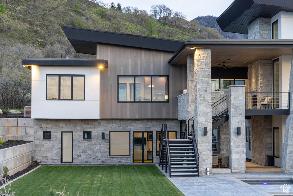 View of front facade featuring ceiling fan, stone siding, stairway, a mountain view, and a front yard