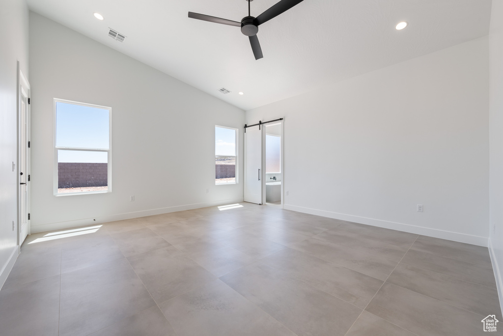 Spare room with finished concrete floors, lofted ceiling, a ceiling fan, baseboards, and a barn door