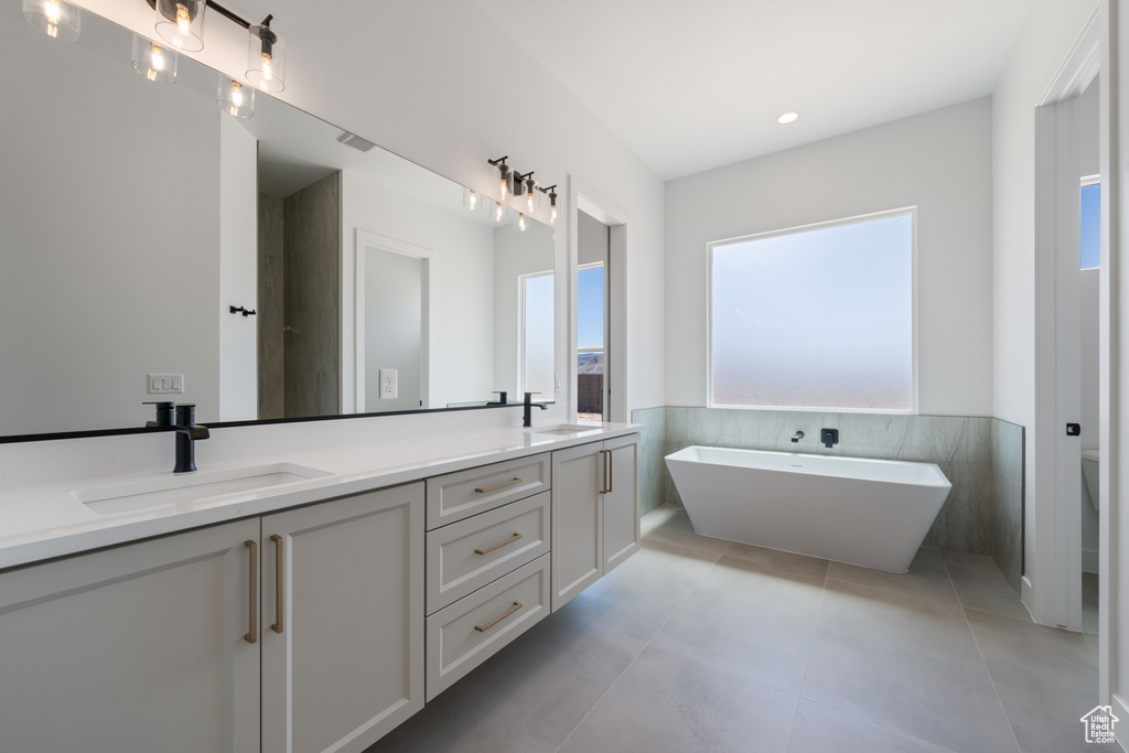 Full bathroom featuring healthy amount of natural light, double vanity, tile walls, a wainscoted wall, and a soaking tub