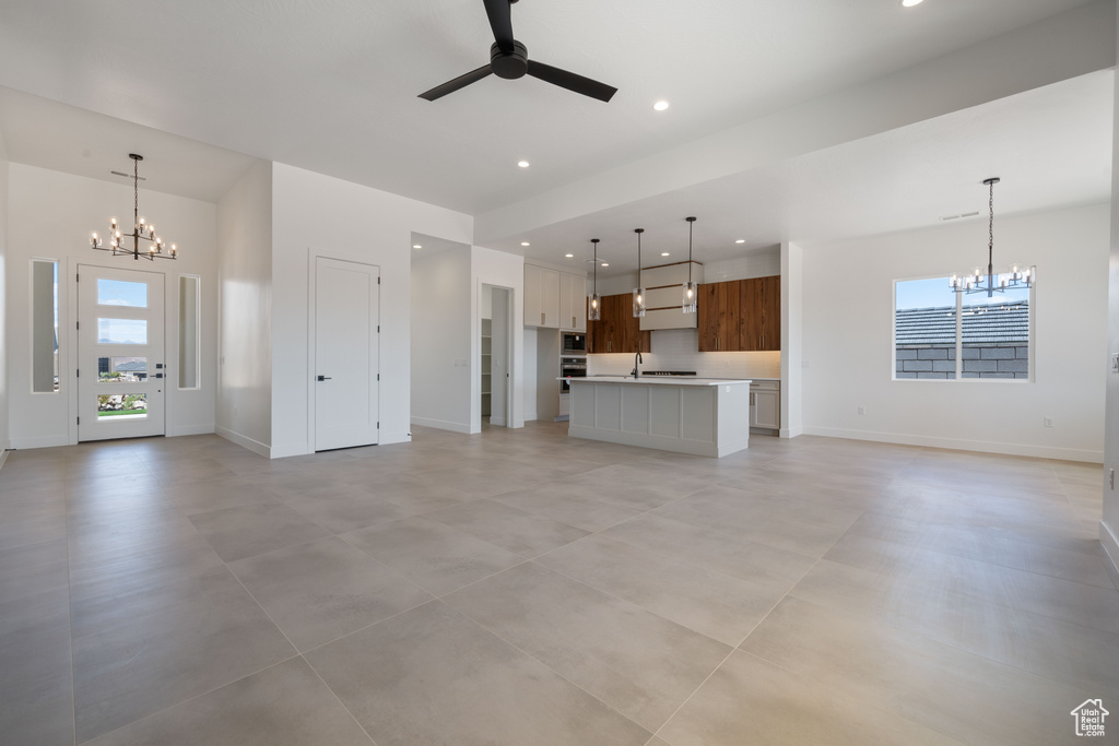 Unfurnished living room featuring a chandelier, ceiling fan, baseboards, recessed lighting, and a sink