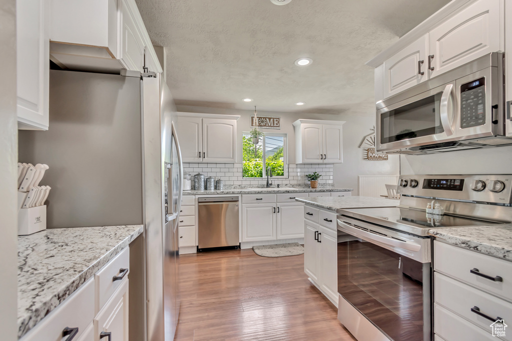 Kitchen with stainless steel appliances, decorative backsplash, white cabinets, light wood finished floors, and recessed lighting