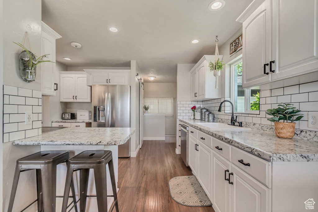 Kitchen with stainless steel appliances, a sink, baseboards, white cabinetry, and a kitchen bar
