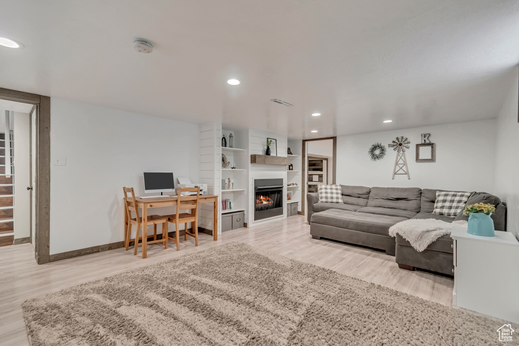 Living area featuring a warm lit fireplace, wood finished floors, recessed lighting, baseboards, and a desk