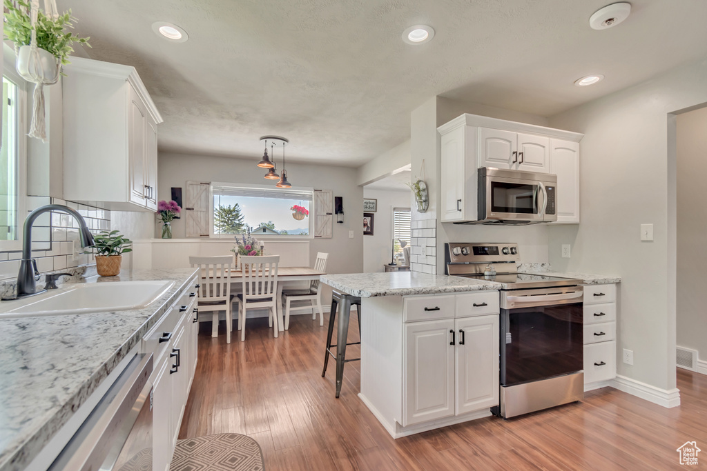 Kitchen featuring appliances with stainless steel finishes, a sink, light wood-style floors, white cabinets, and recessed lighting