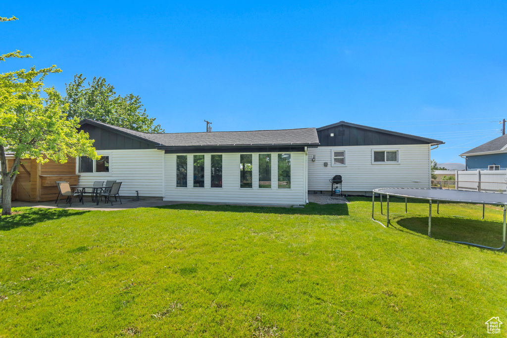 Rear view of property featuring board and batten siding, a trampoline, and a patio area