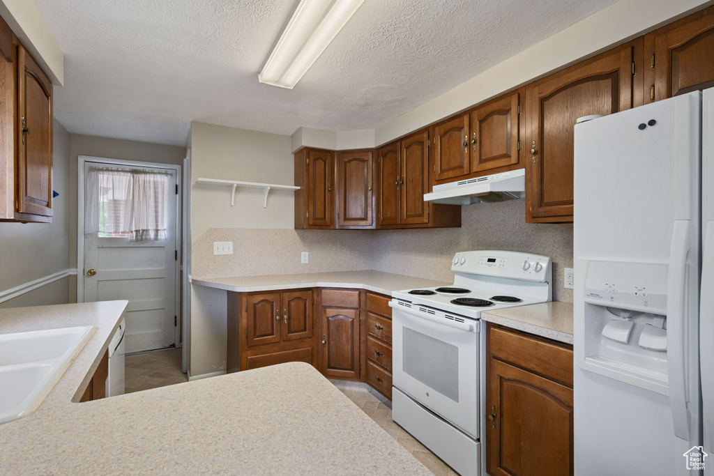 Kitchen with white appliances, under cabinet range hood, a sink, light countertops, and a textured ceiling