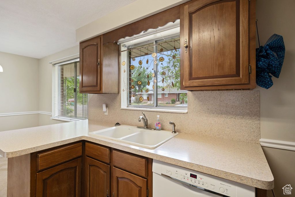 Kitchen with a sink, white dishwasher, a peninsula, decorative backsplash, and light countertops