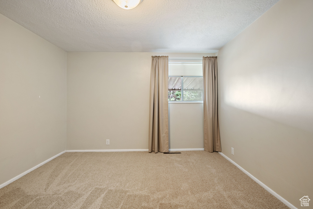 Spare room with a textured ceiling, light carpet, and baseboards