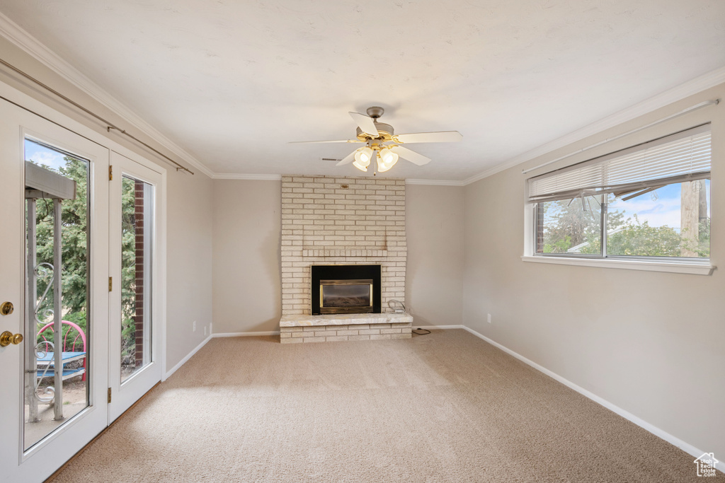 Unfurnished living room featuring a ceiling fan, carpet, baseboards, ornamental molding, and a brick fireplace