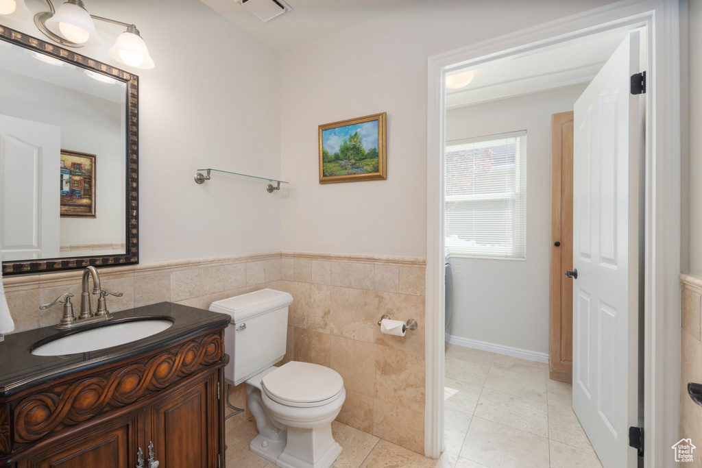 Bathroom with toilet, vanity, tile walls, a wainscoted wall, and tile patterned flooring