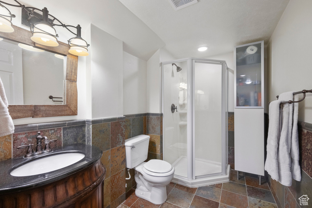 Bathroom with toilet, a stall shower, vanity, tile walls, and stone tile floors