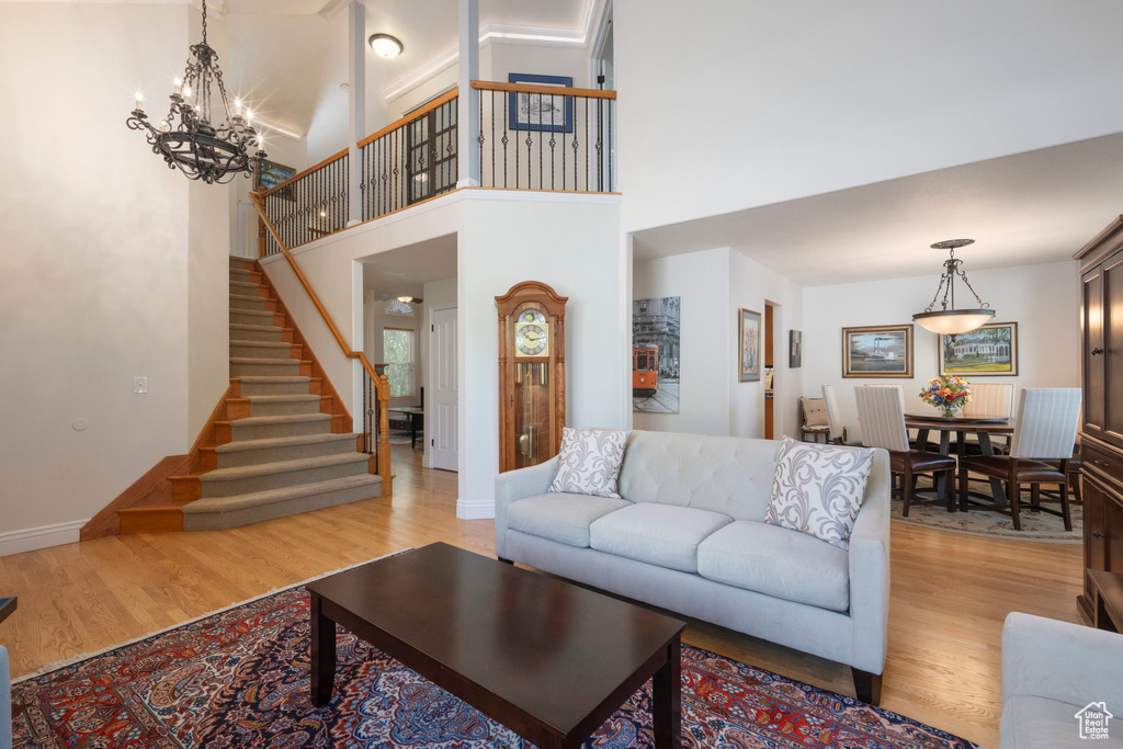 Living room featuring light wood-style floors, stairs, a chandelier, baseboards, and a high ceiling