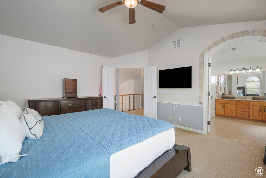Bedroom featuring vaulted ceiling, light colored carpet, arched walkways, connected bathroom, and a sink