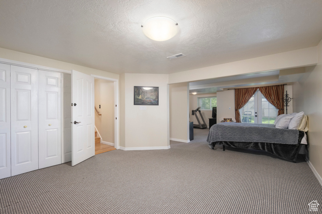 Bedroom with light colored carpet, baseboards, french doors, a textured ceiling, and a closet
