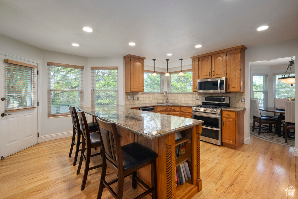 Kitchen featuring stainless steel appliances, a sink, light wood-style flooring, a kitchen bar, and recessed lighting