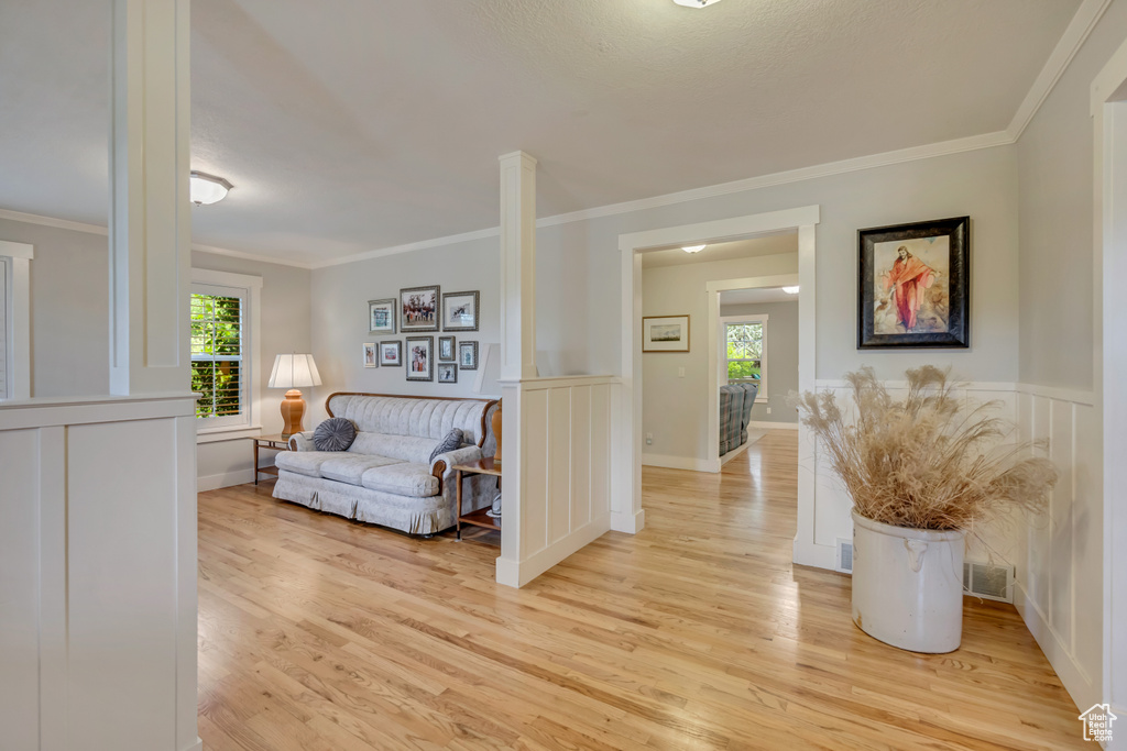 Living area with healthy amount of natural light, light wood-style flooring, ornamental molding, a decorative wall, and wainscoting