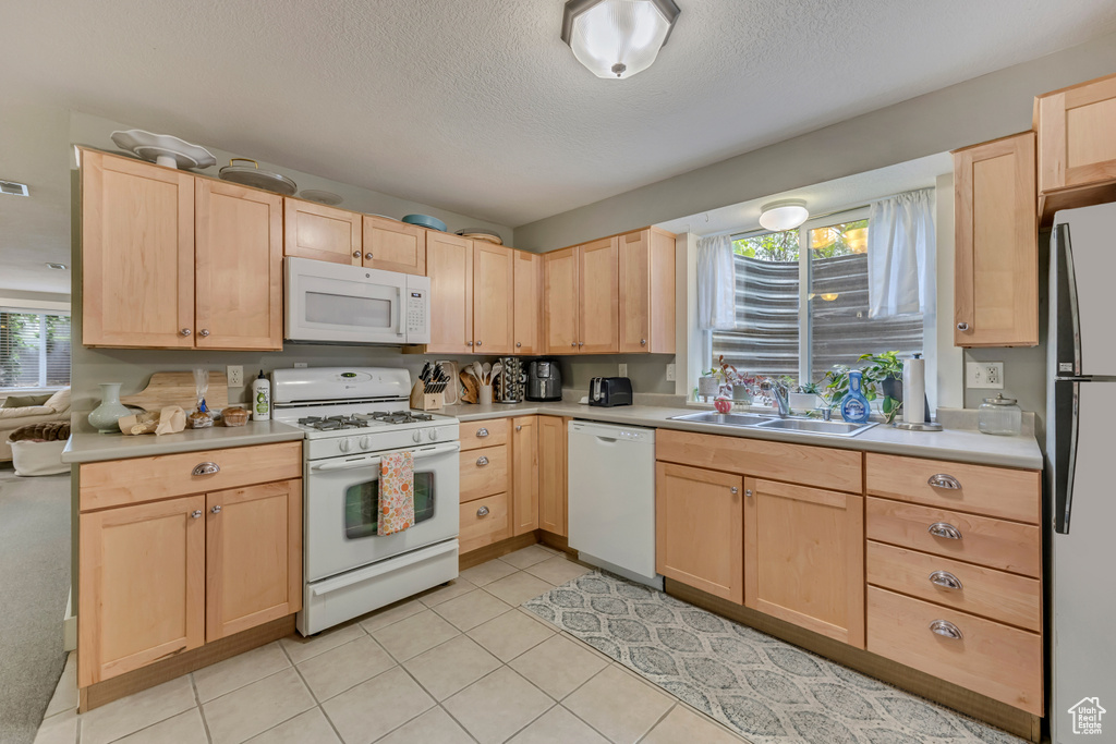 Kitchen featuring white appliances, light brown cabinets, a sink, healthy amount of natural light, and a textured ceiling