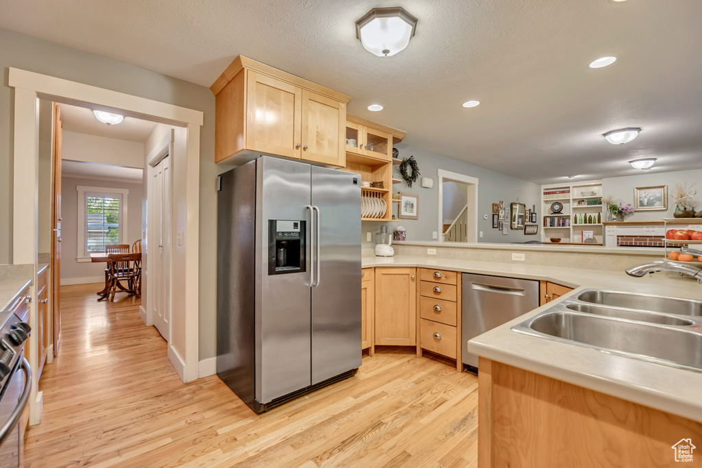 Kitchen with appliances with stainless steel finishes, light brown cabinets, a sink, light wood finished floors, and recessed lighting