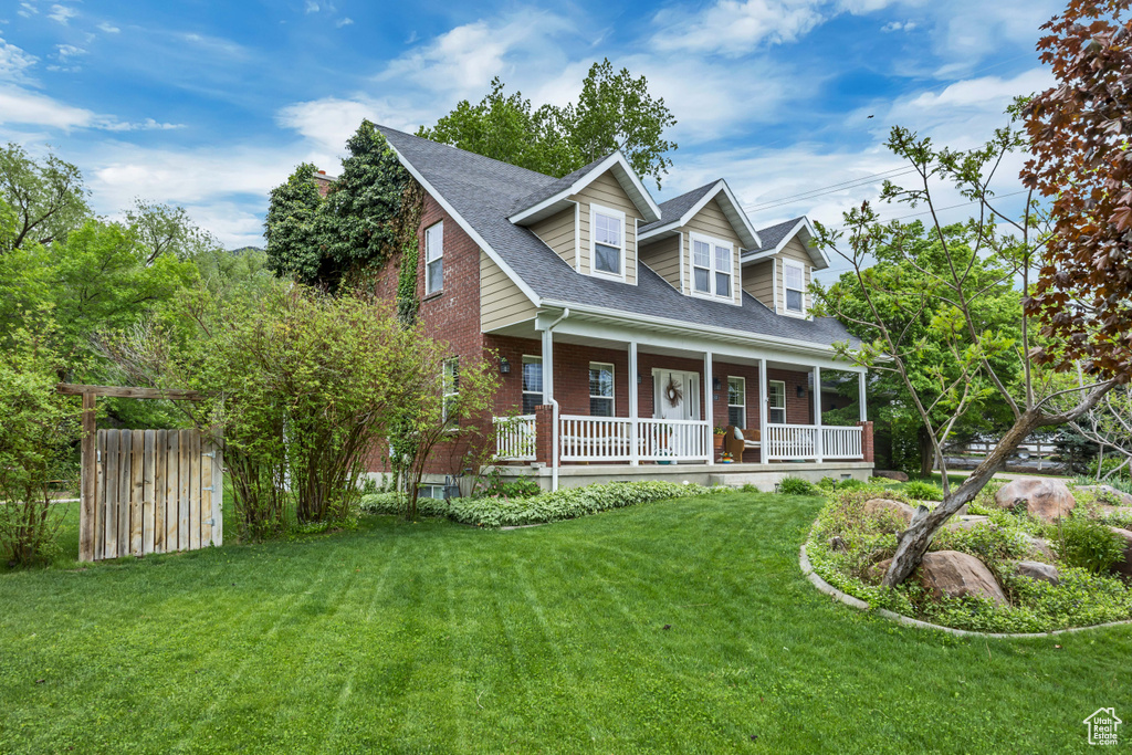 Cape cod-style house with covered porch, a front yard, brick siding, and a shingled roof