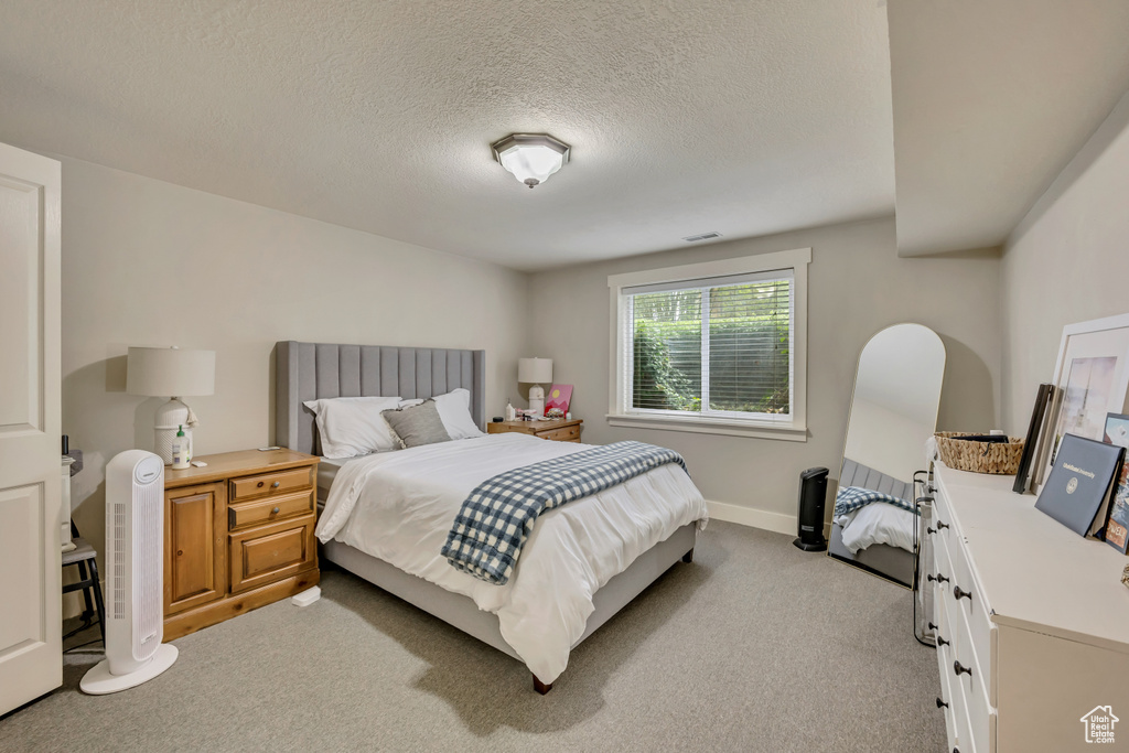 Bedroom featuring light carpet, baseboards, and a textured ceiling