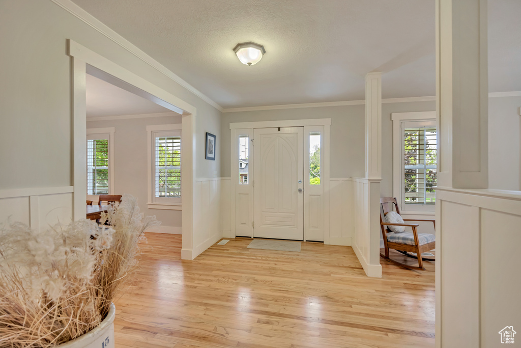 Foyer entrance with light wood-style flooring, ornamental molding, a wainscoted wall, and a decorative wall