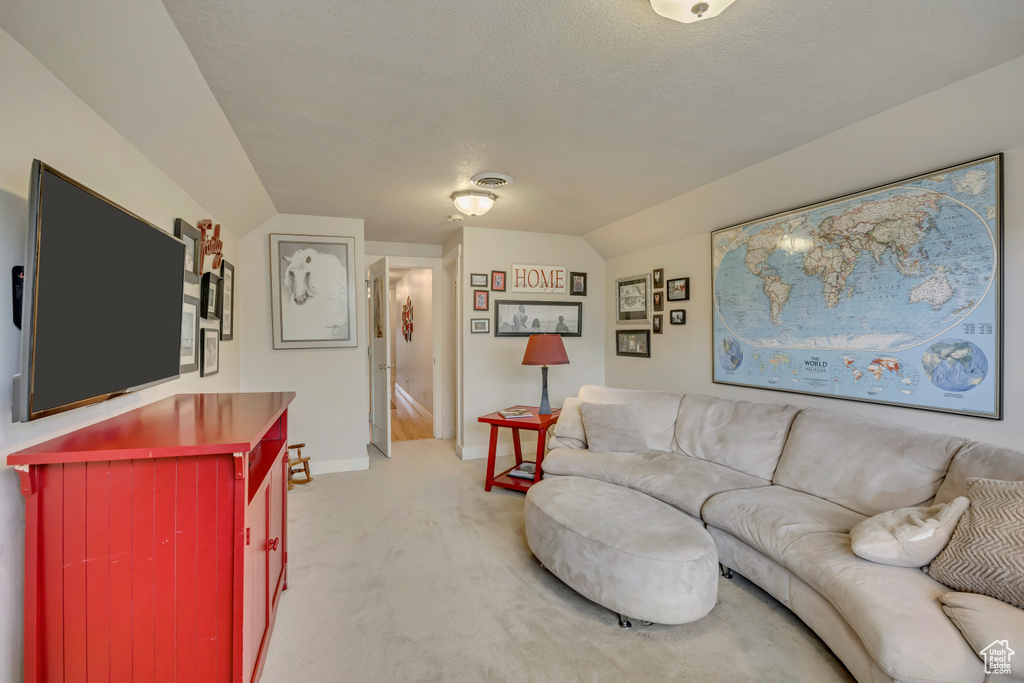 Living area with light colored carpet, vaulted ceiling, baseboards, and a textured ceiling