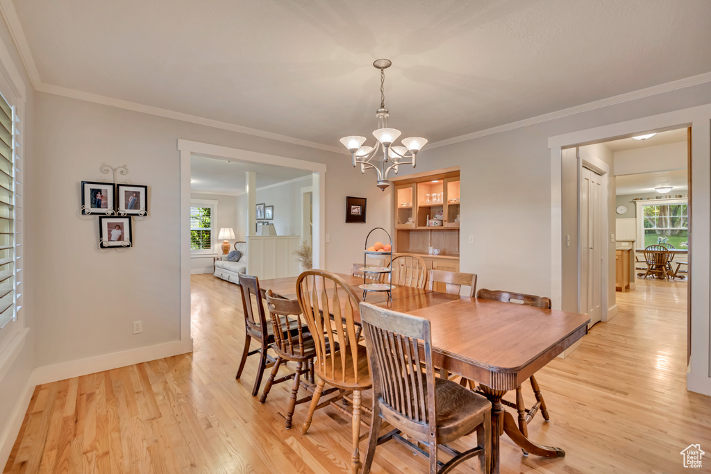 Dining room featuring light wood-style flooring, a chandelier, baseboards, and crown molding