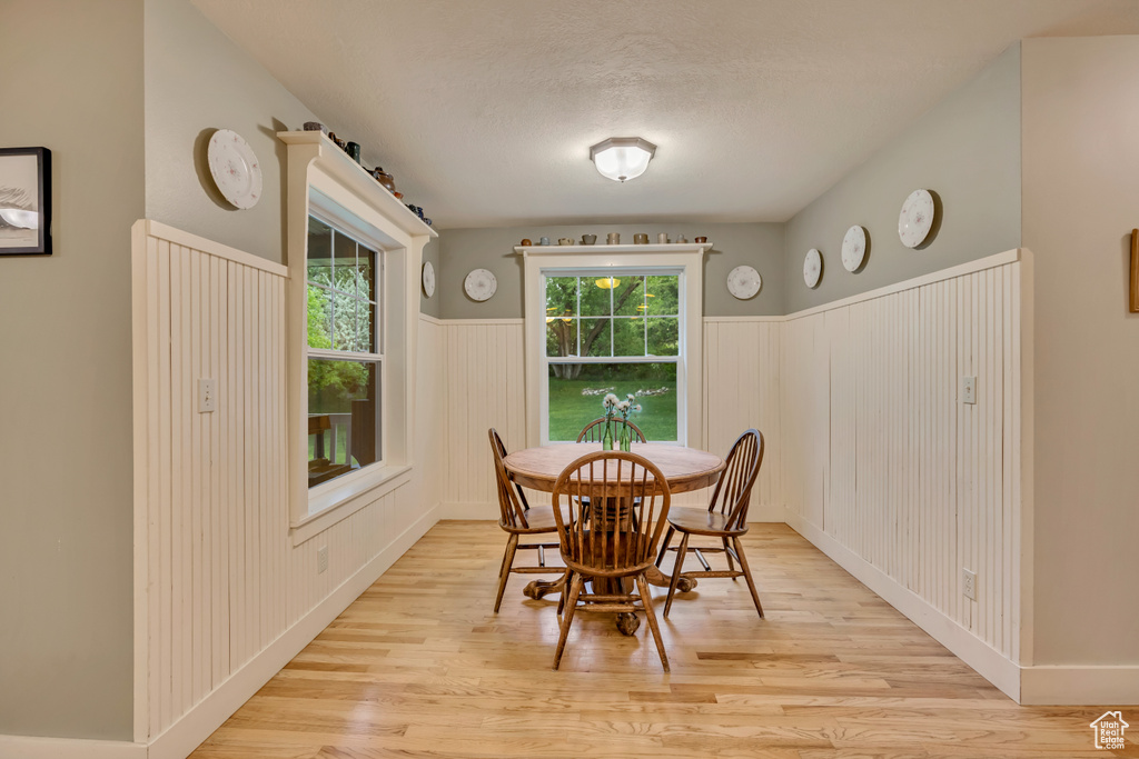 Dining room featuring wainscoting, light wood finished floors, a decorative wall, and a textured ceiling