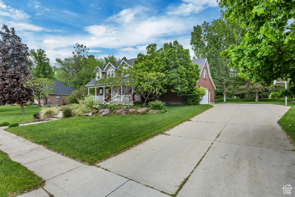 View of front of property featuring covered porch, driveway, a front yard, and a garage