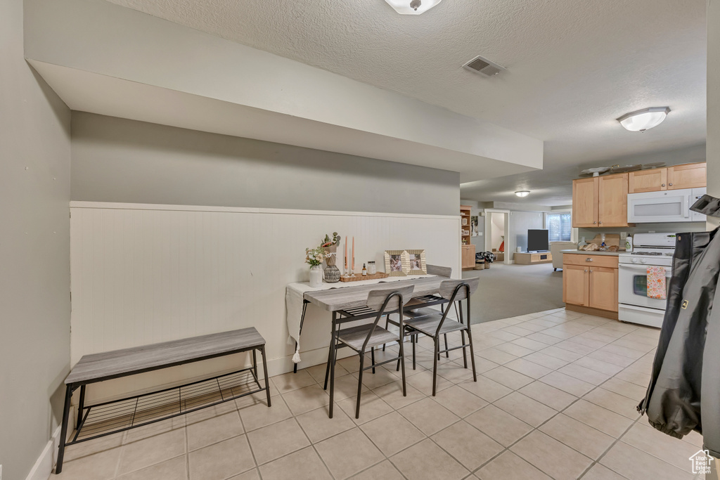 Dining space featuring wainscoting, a textured ceiling, and light tile patterned flooring