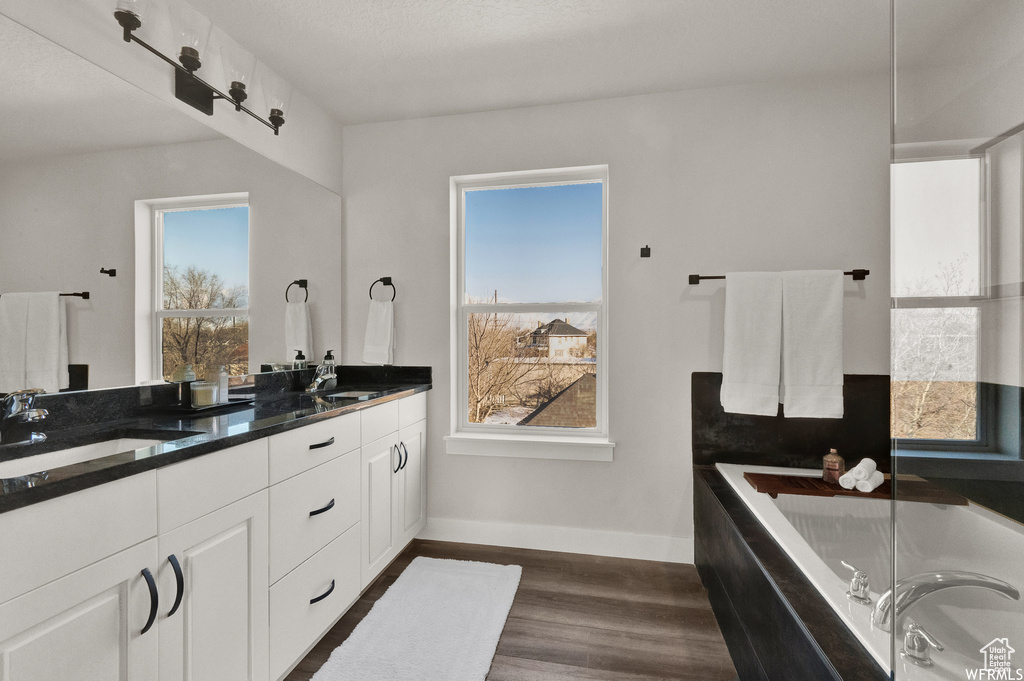 Full bath with wood finished floors, plenty of natural light, double vanity, and baseboards