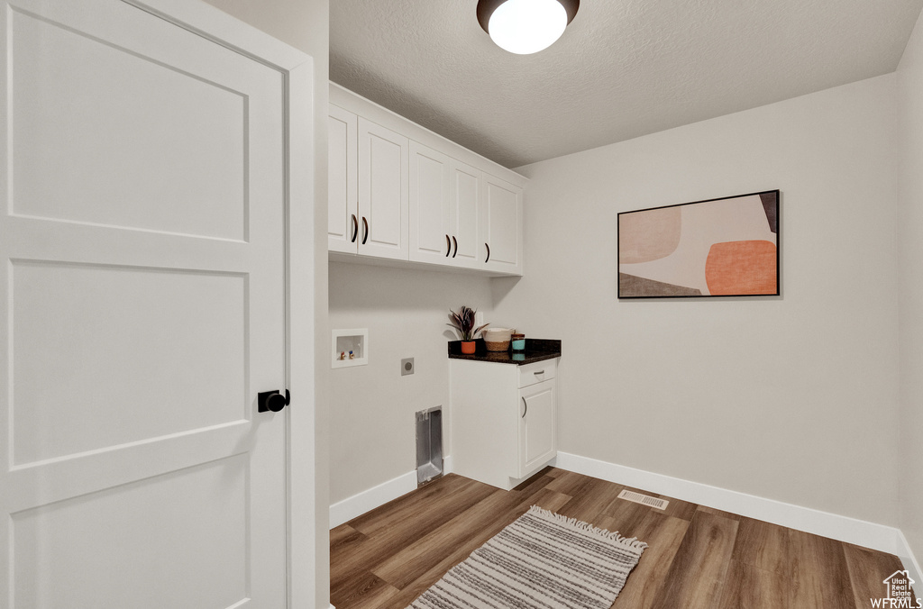 Washroom featuring electric dryer hookup, baseboards, wood finished floors, cabinet space, and hookup for a washing machine