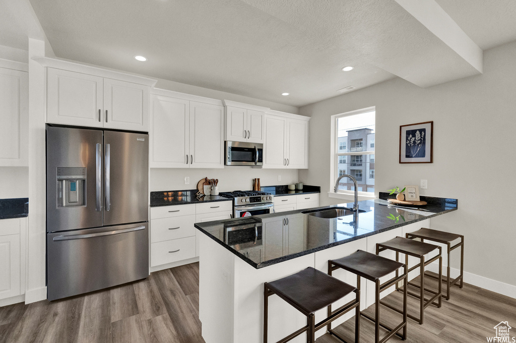 Kitchen with stainless steel appliances, a sink, dark wood finished floors, a kitchen bar, and white cabinets