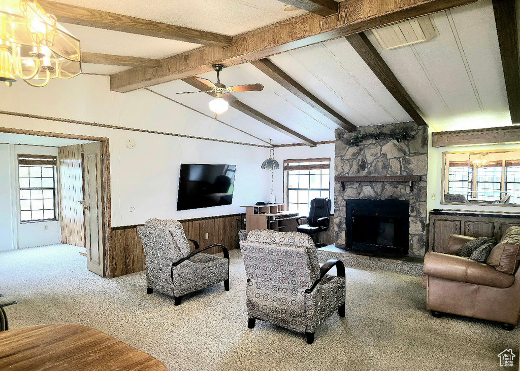 Carpeted living area featuring a stone fireplace, wainscoting, a chandelier, and a ceiling fan