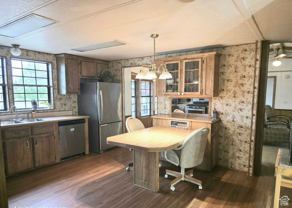 Kitchen featuring appliances with stainless steel finishes, wallpapered walls, a sink, dark wood finished floors, and light countertops