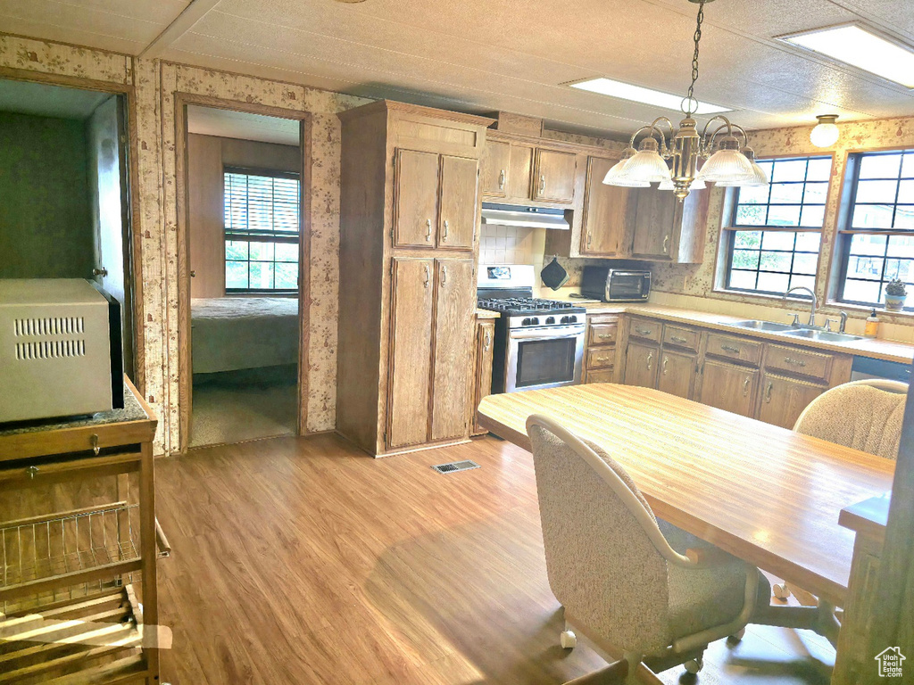 Kitchen featuring stainless steel gas range, a sink, under cabinet range hood, light wood-style floors, and a chandelier