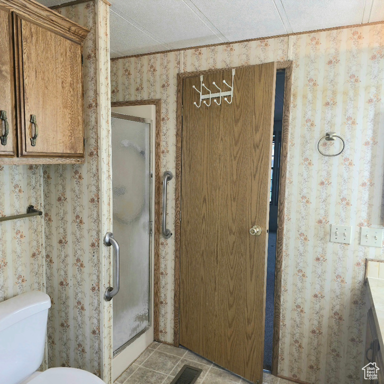 Full bathroom featuring wallpapered walls, a shower stall, toilet, and tile patterned flooring