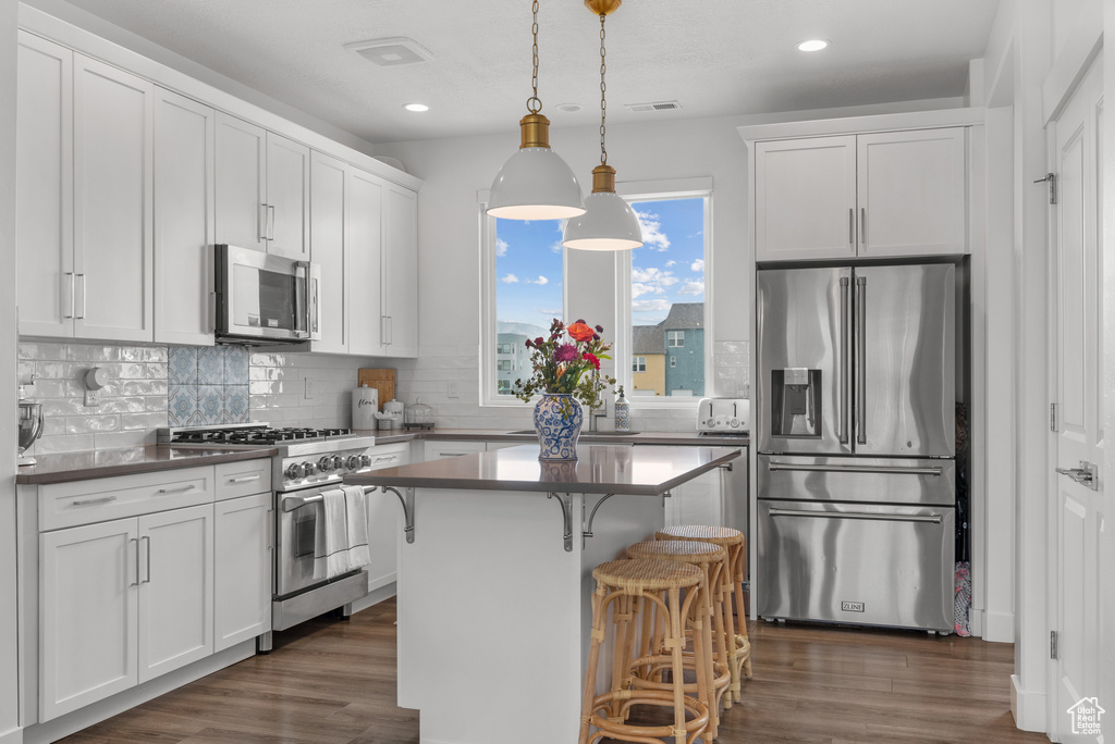 Kitchen with stainless steel appliances, recessed lighting, dark wood-type flooring, white cabinets, and a breakfast bar area